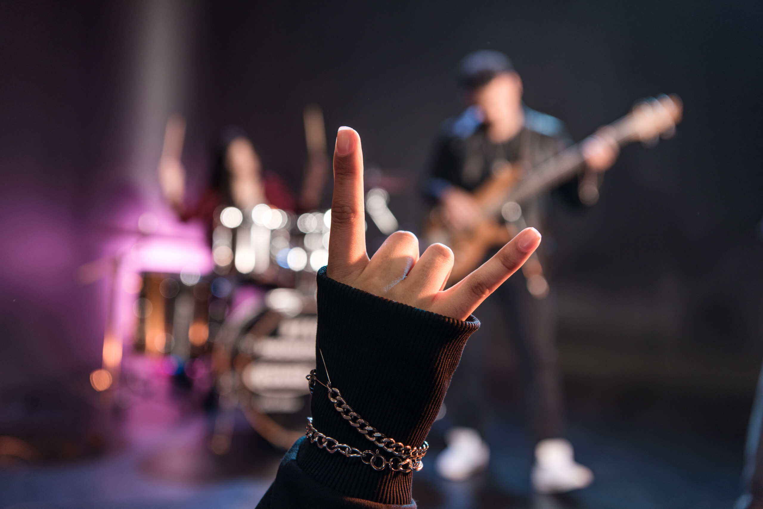 Person showing sign of the horns while rock band playing on stage