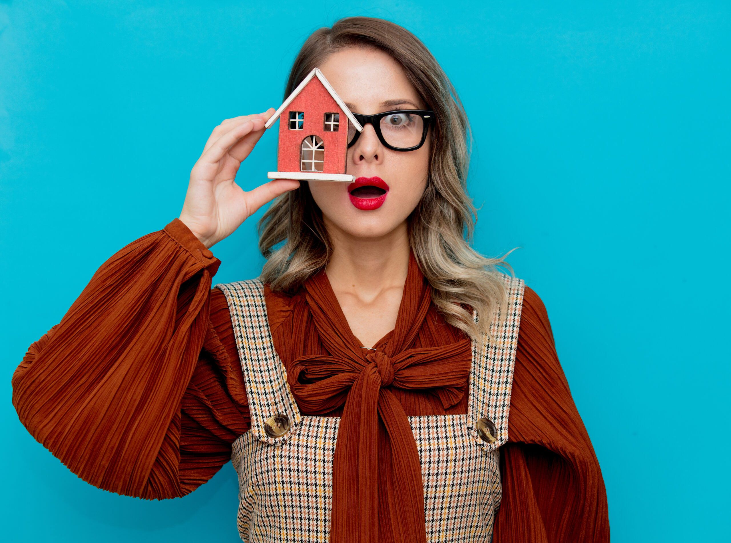 Youn woman with toy house on blue background